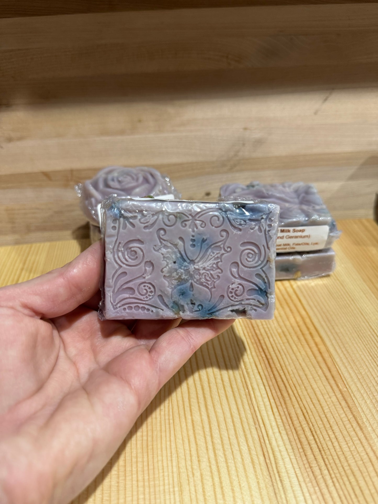 Purple floral shaped goat milk soap bars stack on wood background.