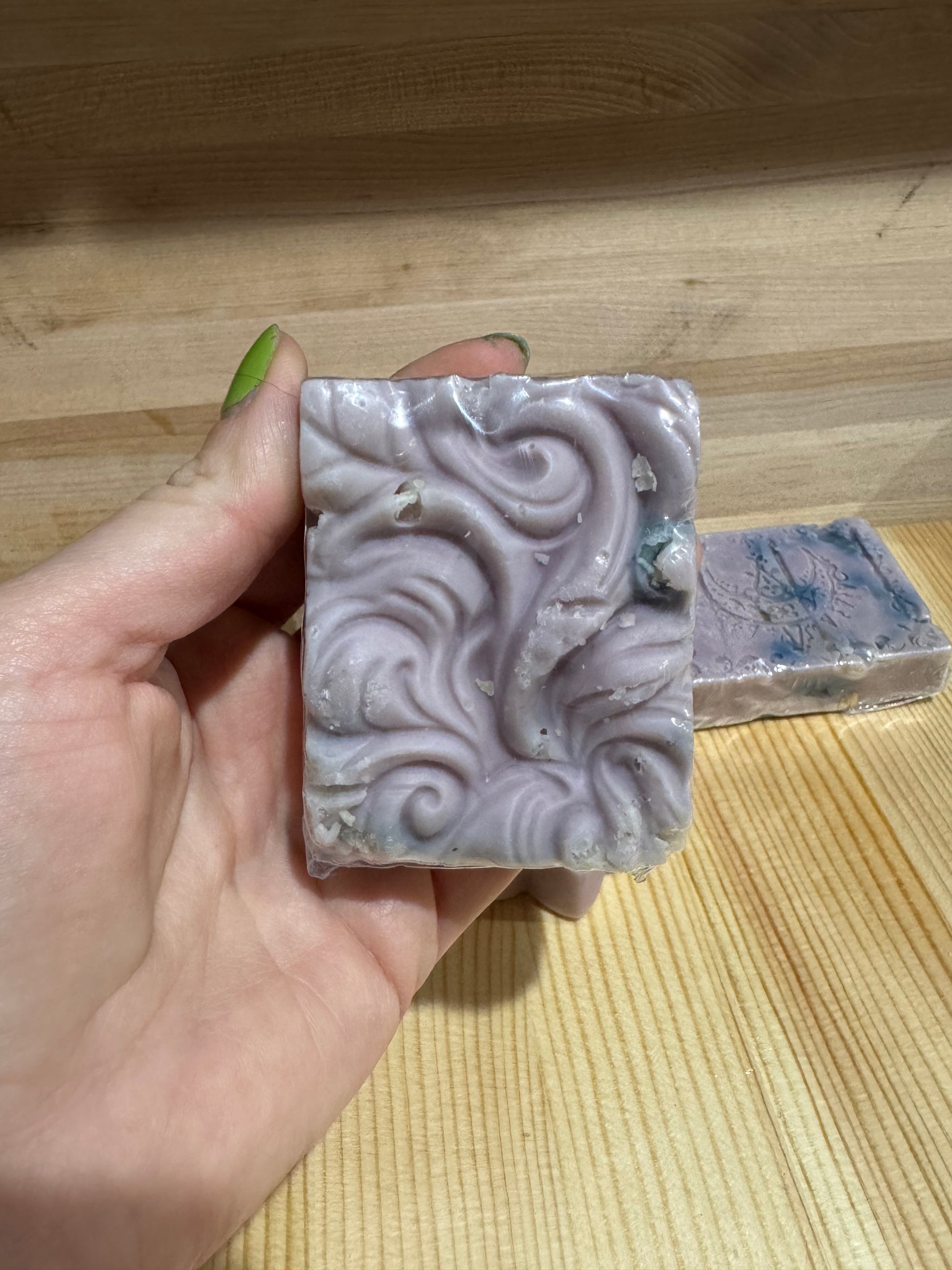 Hand holding a bar of soap with decorative design against a wooden background