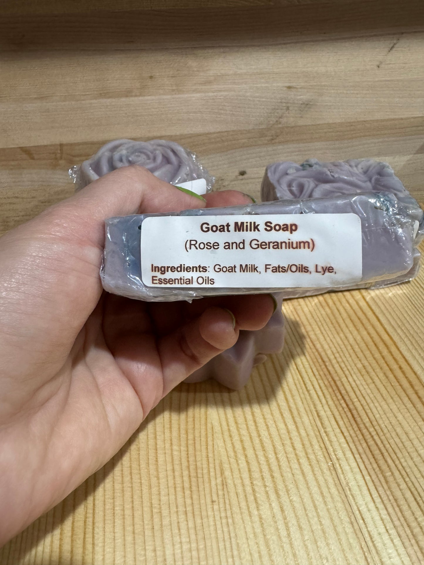 Hand holding a bar of purple goat milk soap with the ingredients label showing