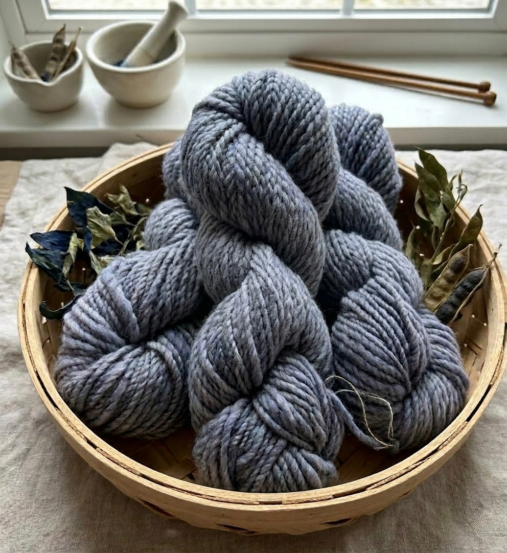 Blue-gray yarn skeins in a woven basket on a light surface with a window in the background