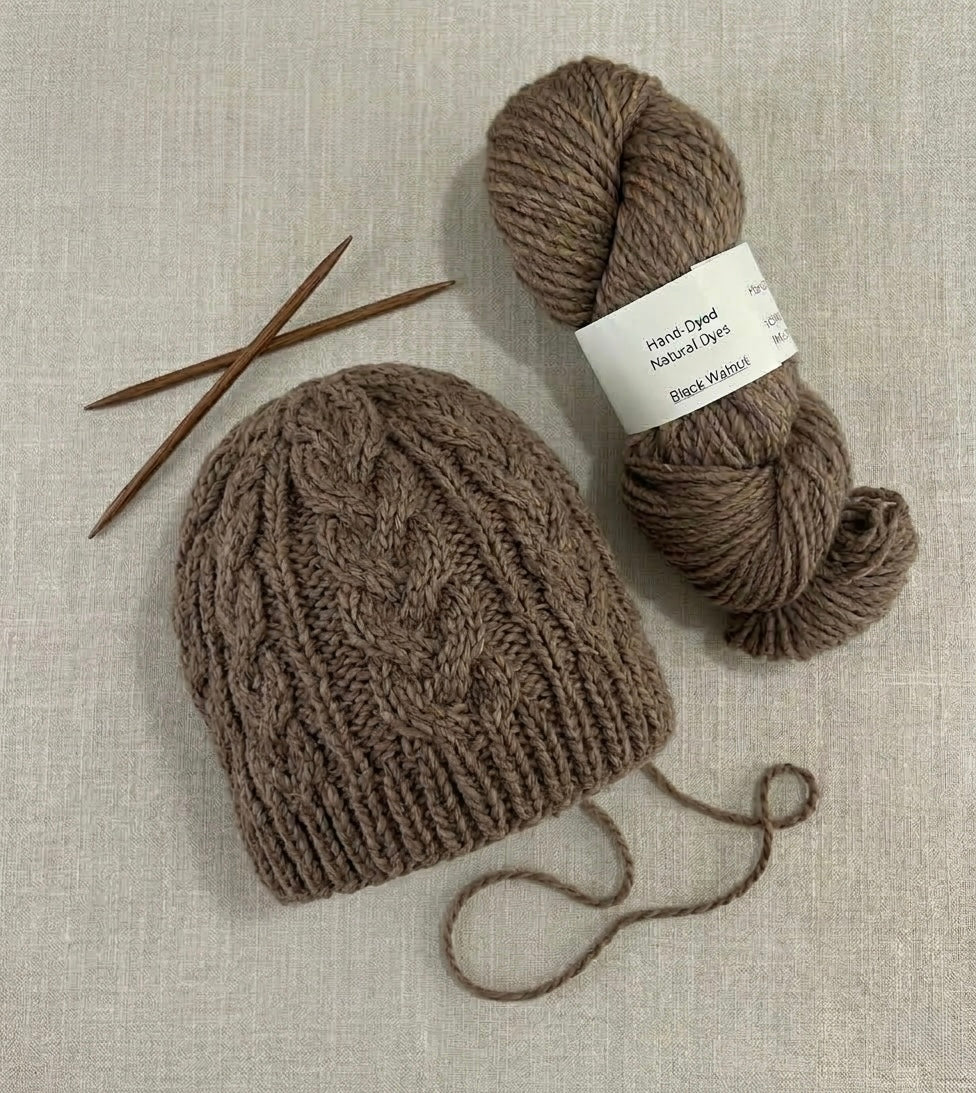 Knitted brown hat with yarn and needles on a textured beige background