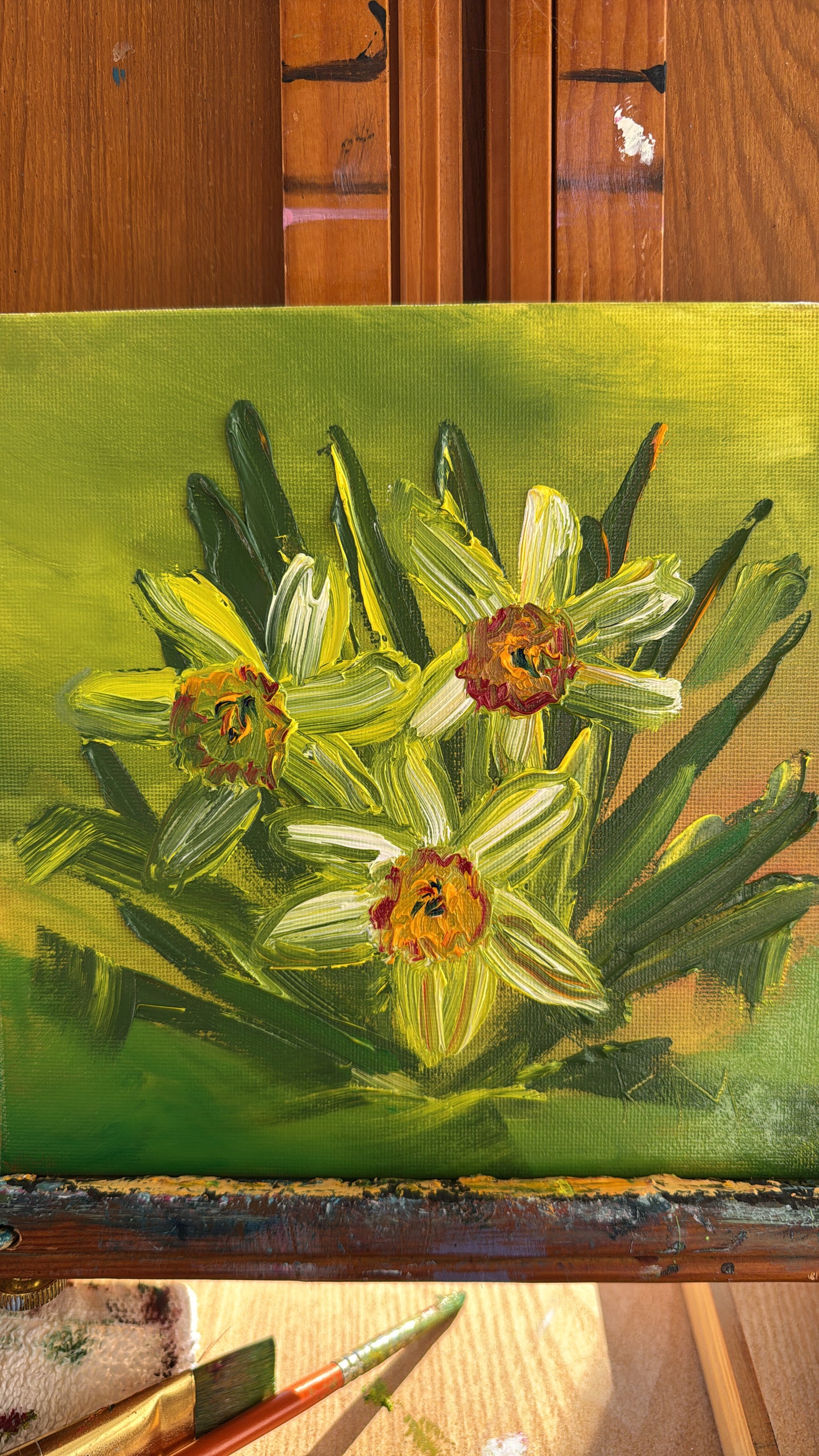 Close-up of an original daffodil oil painting with thick impasto texture, featuring three yellow-green flowers and green leaves on a lime green background.