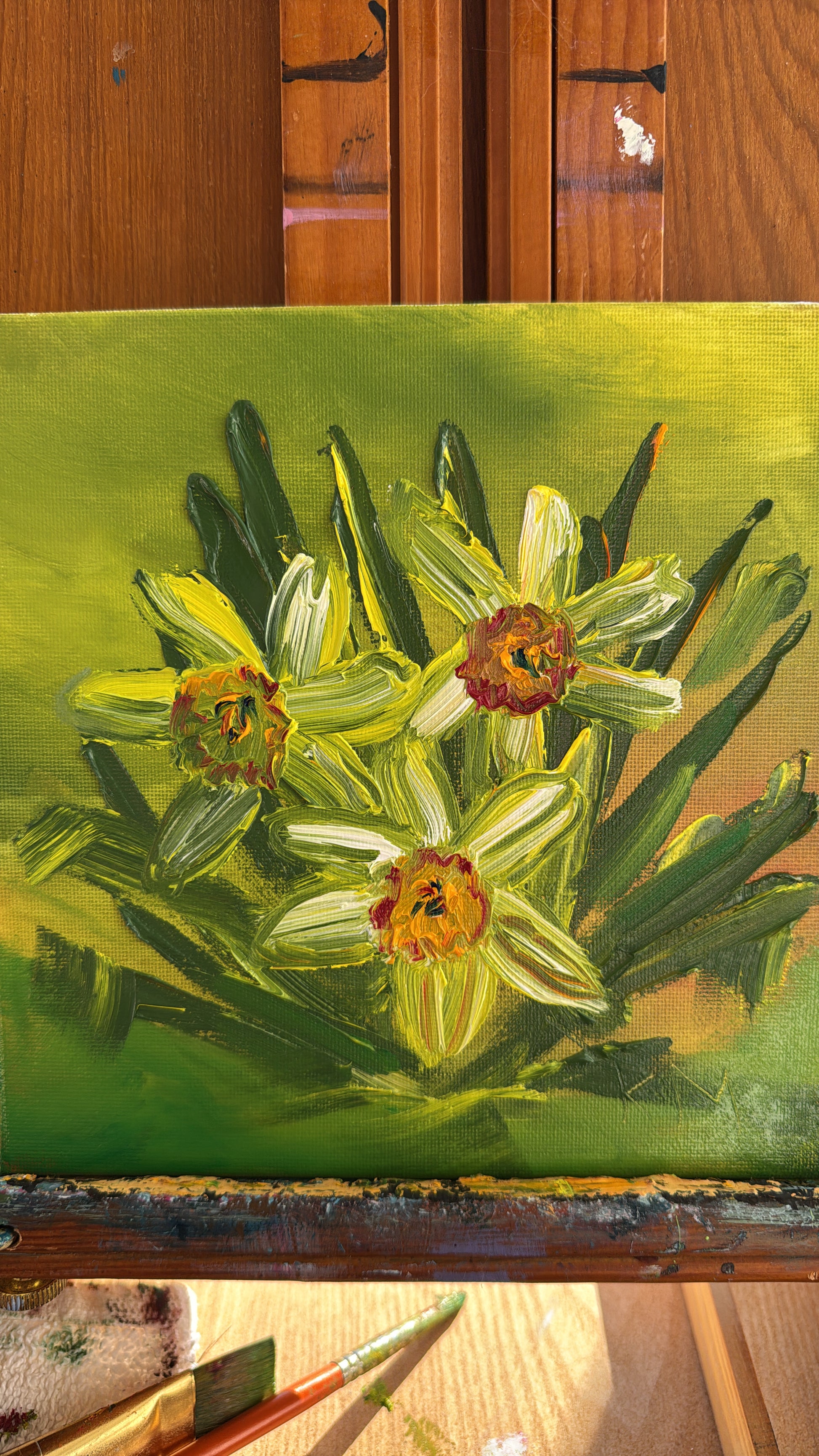 Close-up of an original daffodil oil painting with thick impasto texture, featuring three yellow-green flowers and green leaves on a lime green background.